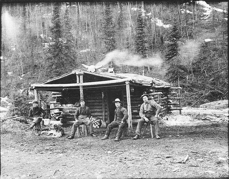 Four men and dog sitting in front of log cabin, Hunker Creek, 1899